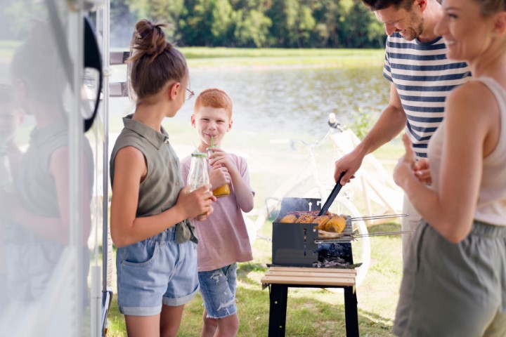 family grilling beside camping vehicle and lake