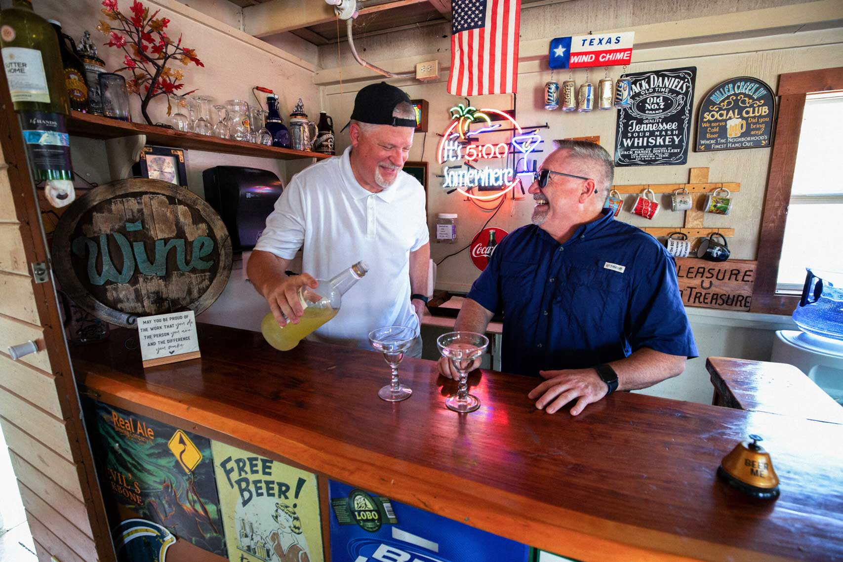 Two friends sharing a laugh and drinks at a bar setup in Johnson City campgrounds, surrounded by vintage decor and memorabilia