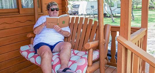 an elderly woman relaxing with a book on a rocking chair at a cabin in a Johnson City, TX camping ground