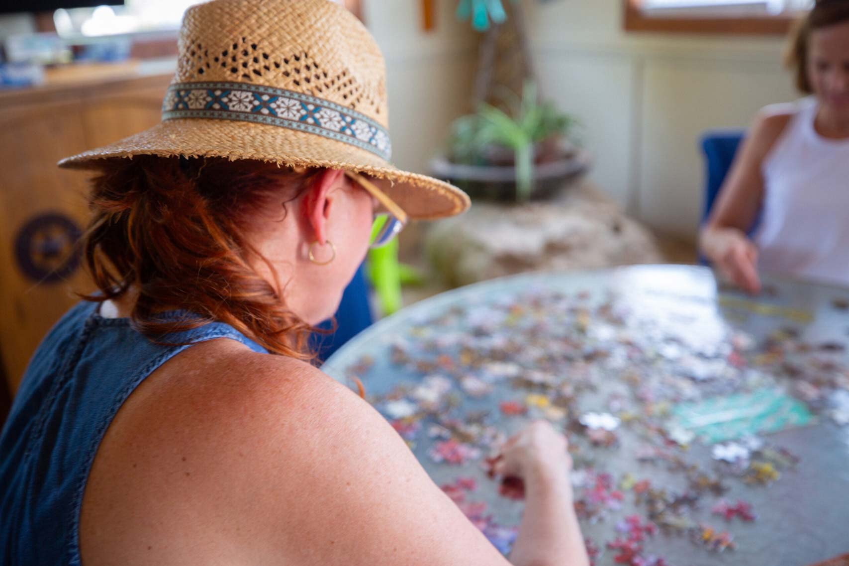 A woman wearing a straw hat assembling a puzzle, enjoying a recreational activity at a long-term RV park near Austin, TX