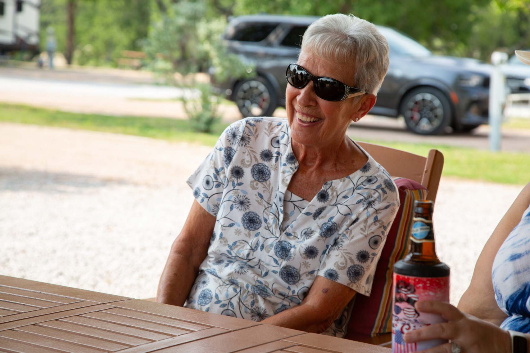 A cheerful senior woman enjoying a social gathering at a long-term RV park near San Antonio, TX, with RVs and trees in the background