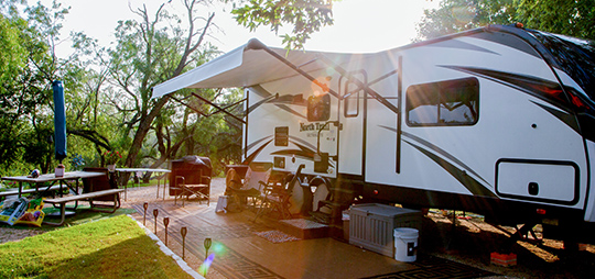 Spacious RV site at a park around San Antonio, Texas, with a large RV and outdoor seating area bathed in the warm glow of a setting sun