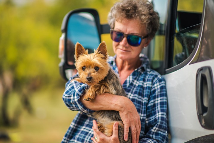 an old woman reeling on an rv holding a pet dog