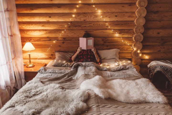 woman reading book in log cabin bed