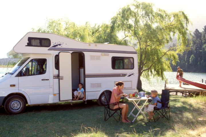 A family enjoying a camping trip by a lake with a motorhome parked nearby