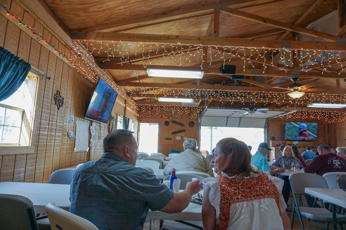 People seated at tables in a spacious indoor hall decorated with string lights and wooden walls