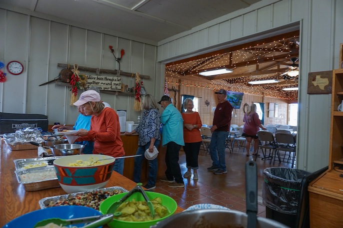 Group of people gathered around a buffet table filled with various dishes in a decorated indoor space with string lights and rustic decor