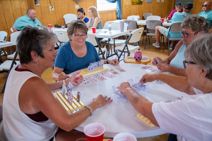 Group of women playing a card game around a table in a bright indoor hall, smiling and enjoying the game