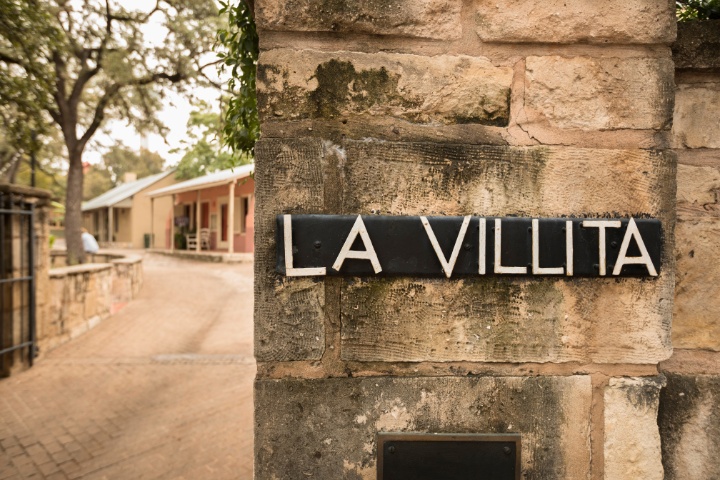 Entrance to the La Villita Historic District in San Antonio, with a stone wall featuring a black and white sign marking the historic site