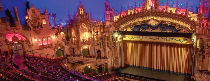 A view of the grand stage inside the Majestic Theatre, showcasing its elaborate decor, velvet curtains, and rows of theater seating