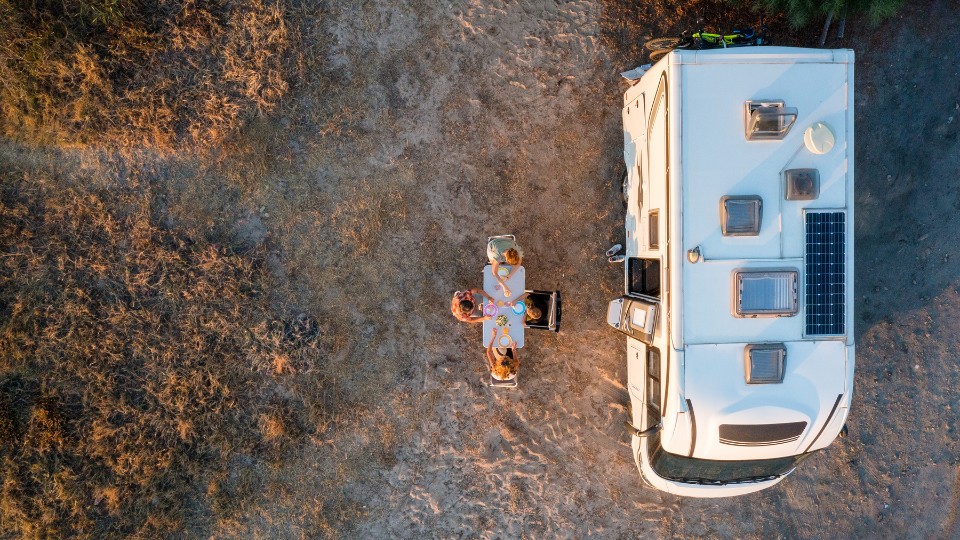 Top-down view of an RV parked beside a picnic table with people enjoying an outdoor meal