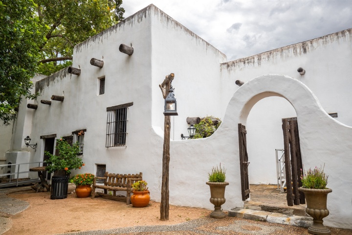 The historic Spanish Governor’s Palace in San Antonio, showcasing its distinct adobe walls, wooden accents, and tranquil outdoor seating area