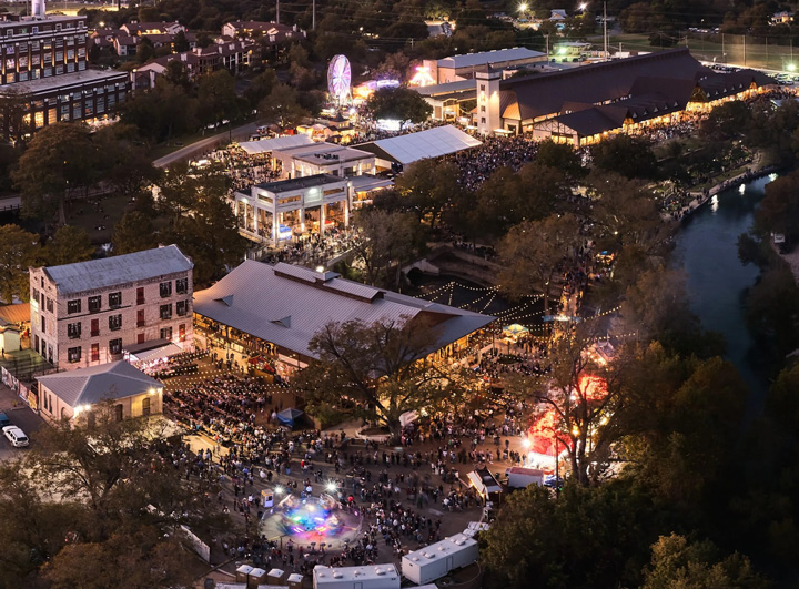 Aerial view of Wurstfest in New Braunfels, showcasing the festival grounds, lively crowds, colorful lights, and carnival rides