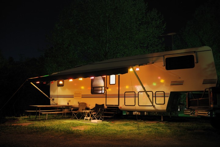 A camper van parked at a campsite at night, lit by colorful string lights