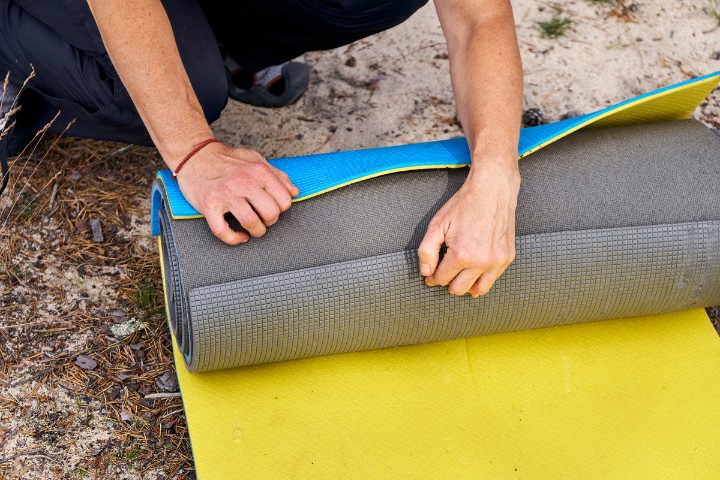 Person rolling up a gray and yellow outdoor mat during a camping trip