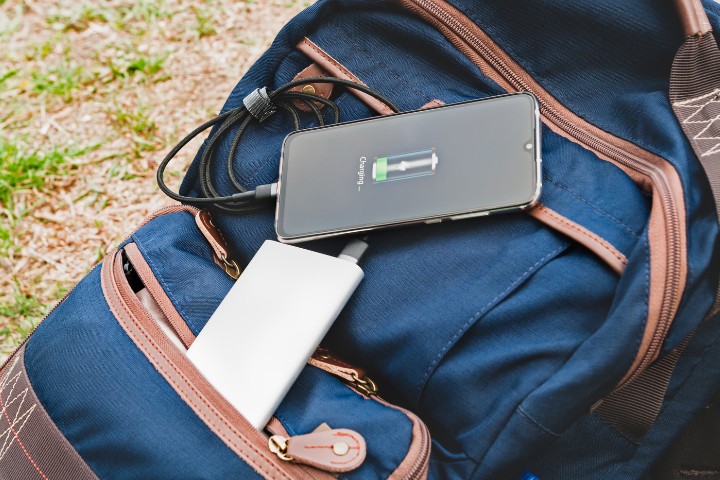 Portable power bank charging a smartphone on a backpack outdoors