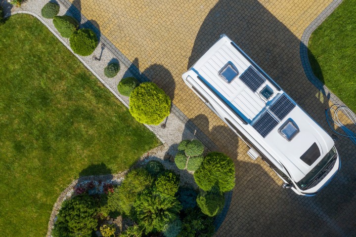 Solar-powered RV parked on a stone driveway surrounded by greenery, viewed from above.