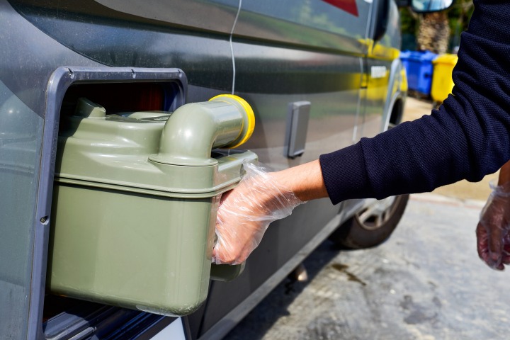 Rver removing an RV waste tank for disposal while wearing gloves