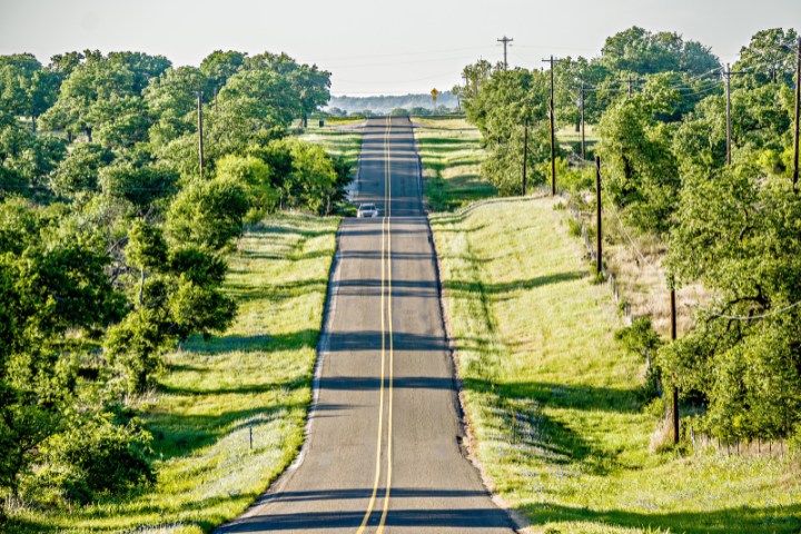 Straight scenic road surrounded by lush greenery on the Willow City Loop in Texas Hill Country, a popular route for motorcyclists