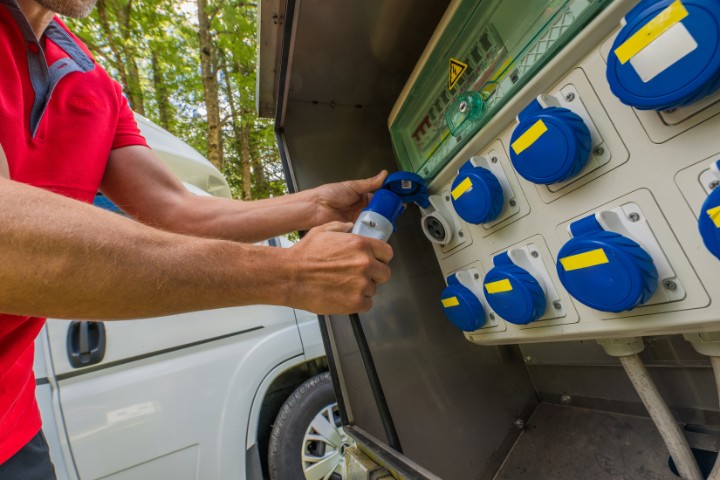 Close-up of hands plugging into a power station for RV hookups during camping