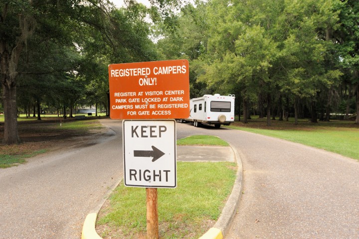 RV entering a campground with signage outlining rules for registered campers and a directional arrow.