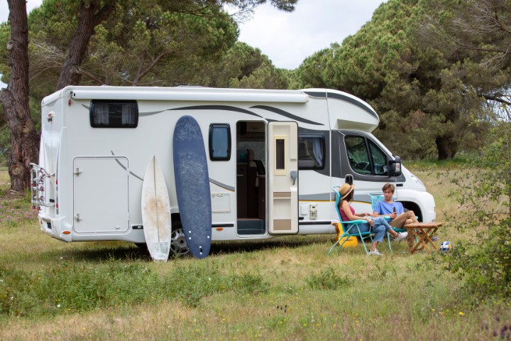 Couple relaxing outside an RV parked in nature, with surfboards leaning against the vehicle