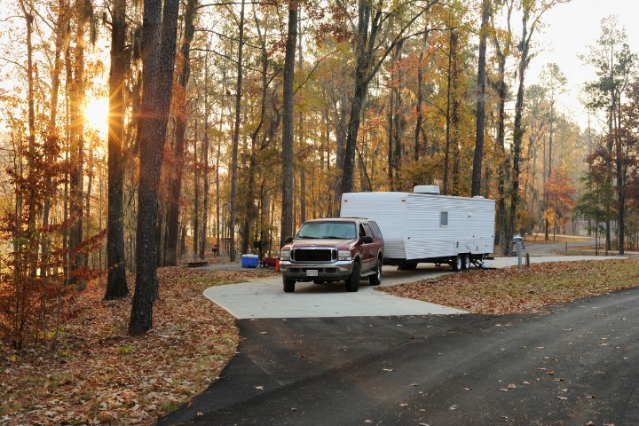 RV campsite featuring an RV trailer and a red truck surrounded by fall foliage in a peaceful wooded area