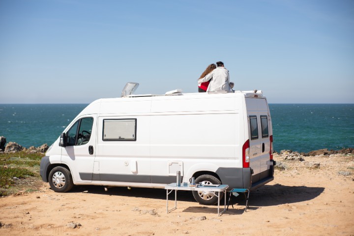 couple sitting on the roof of their camper van by the ocean, embracing the RV lifestyle