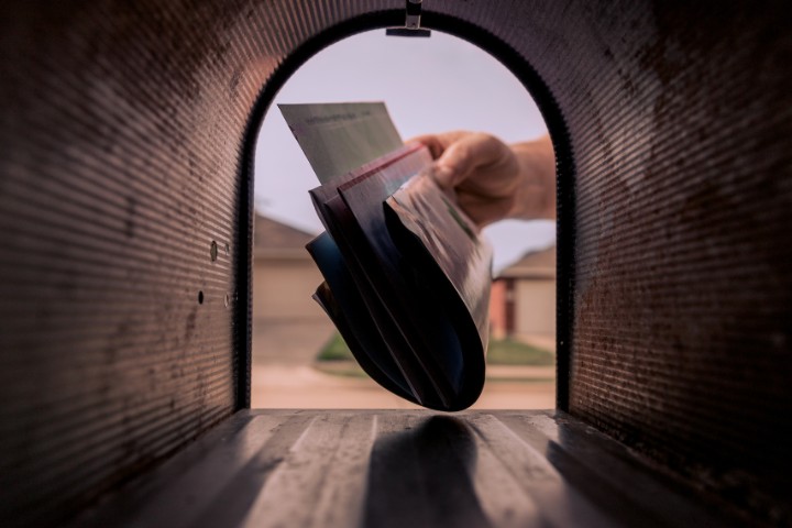 A close-up of a hand placing mail in a mailbox, representing mail forwarding options for RVers