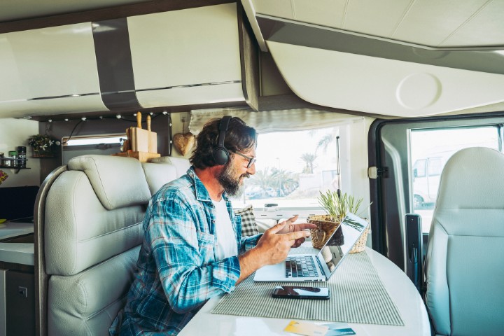 A man with headphones working on his laptop in an RV, highlighting the digital nomad lifestyle