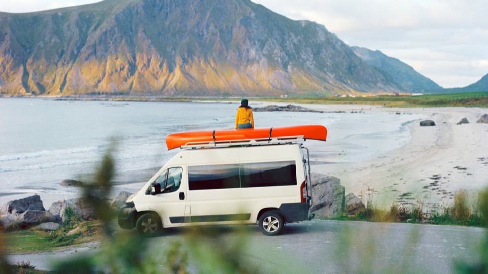 Woman sitting on top of a camper parked by the lake, capturing the freedom of RV road trip adventures