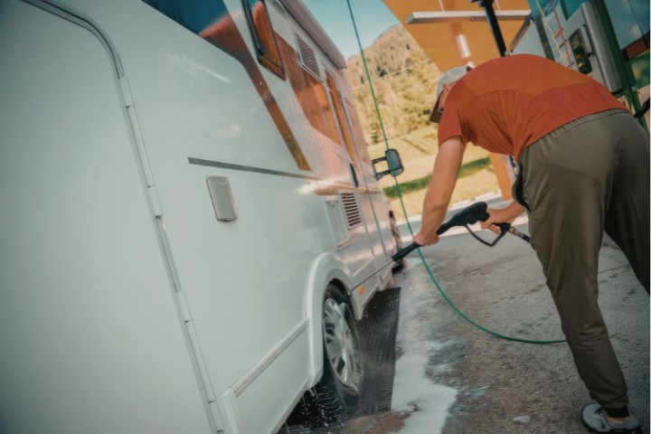 RV traveler washing the side of a camper after stopping at a fuel station