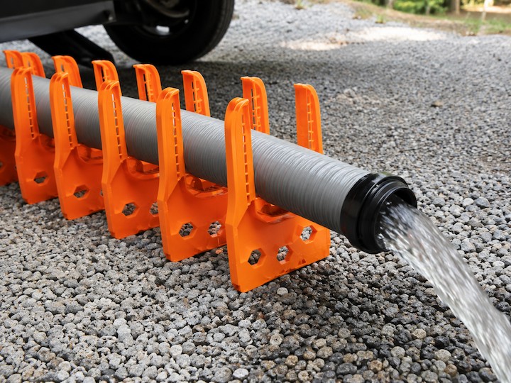 Orange RV sewer hose support holding a gray drainage hose over gravel at a campsite