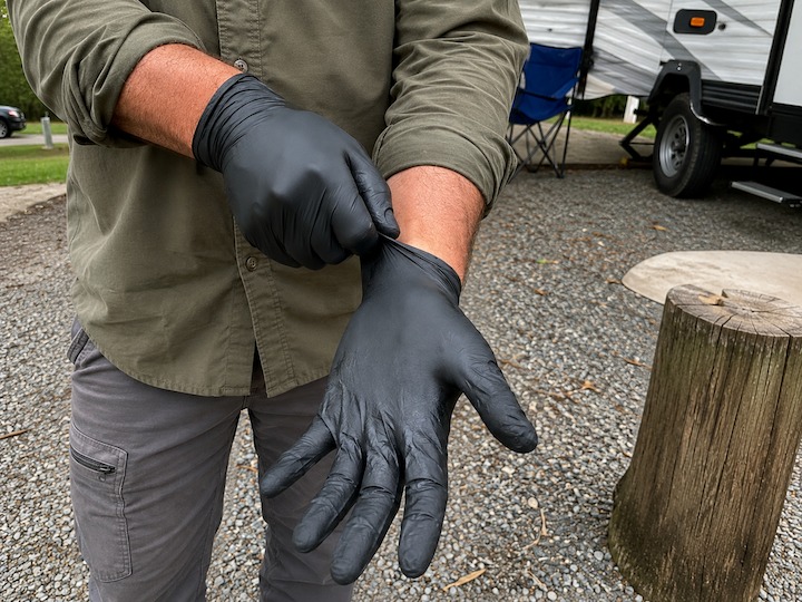 Man putting on black disposable nitrile gloves at an RV campsite