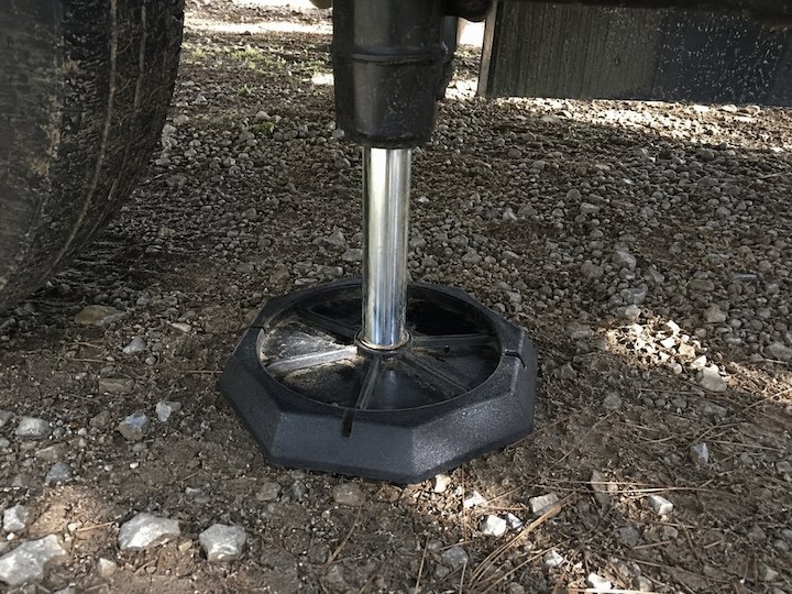 Black RV jack pad supporting a trailer stabilizer on uneven gravel ground