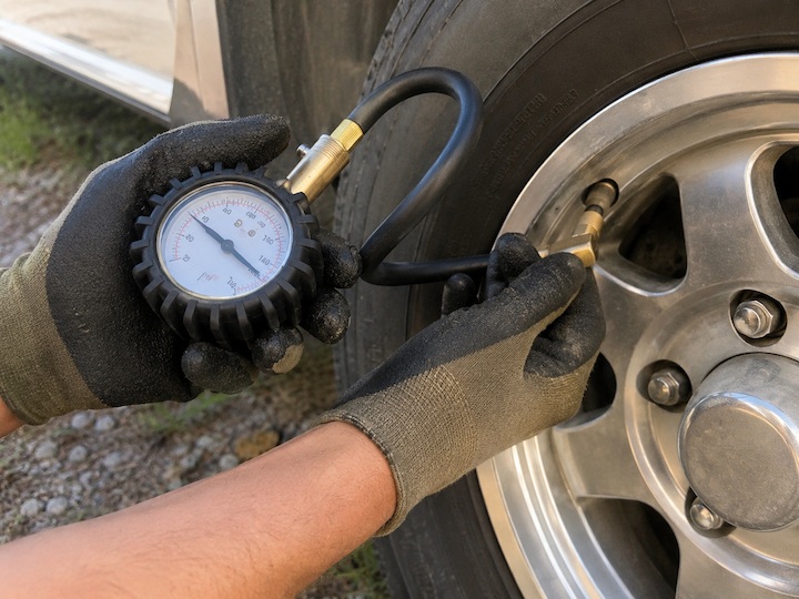 Gloved hands using a tire pressure gauge to check the air pressure on an RV tire