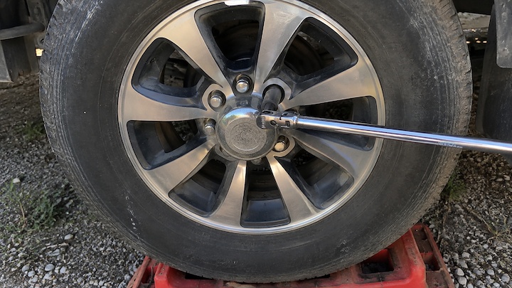 Torque wrench tightening lug nuts on an RV trailer wheel at a gravel campsite