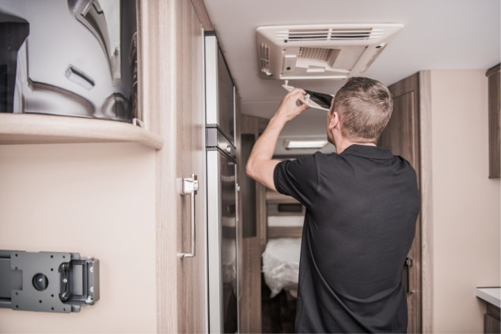 RV owner replacing the ceiling air conditioner filter inside a travel trailer