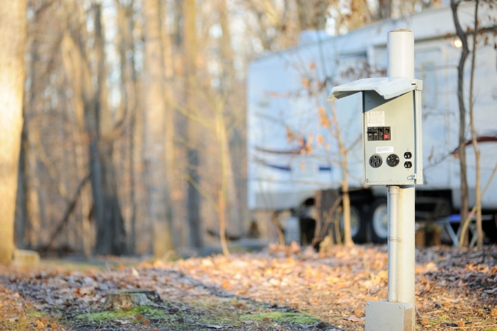 RV campground electrical hookup panel beside a travel trailer at a wooded campsite